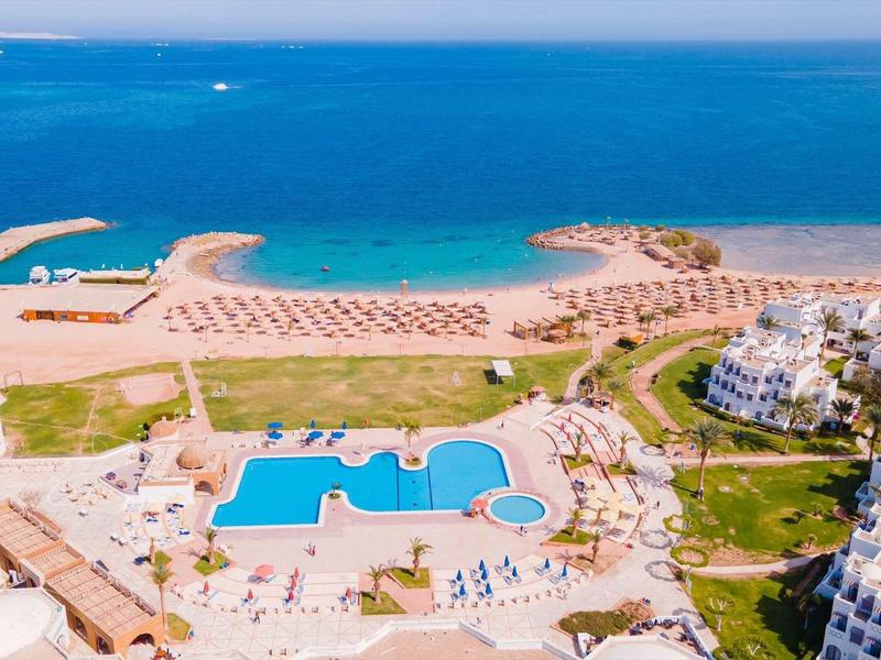 Luftaufnahme eines Resorts mit Pool, Sonnenschirmen und Sandstrand am türkisblauen Meer.