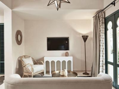 Heller Wohnzimmerraum mit weißem Sofa, Sessel, stehendem Lampenlicht und Wandfernseher.