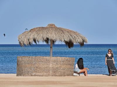 Strand mit Strohmantel-Sonnenschirm und zwei Frauen am klaren blauen Wasser