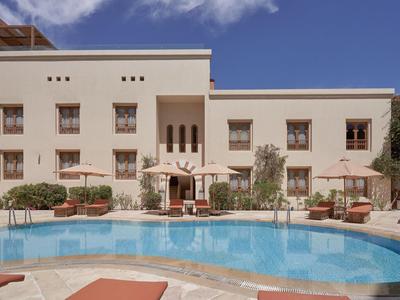 Fasáda hotelu v pouštním stylu a čistý bazén pod modrou oblohou.