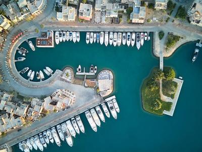 Luftaufnahme eines Hafens mit Booten, Gebäuden und einer kleinen bewachsenen Halbinsel im Meer.