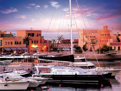 Yachten liegen ruhig im Hafen vor orangefarbenen Gebäuden bei Sonnenuntergang.