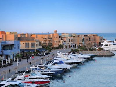 Hafen mit vielen Booten, modernem Kai und Gebäuden unter blauem Himmel bei Sonnenuntergang.