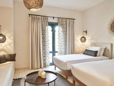 Helles Schlafzimmer mit zwei Einzelbetten, runden Tischen und warmen Beleuchtungselementen.