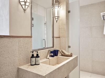 Modernes Badezimmer mit großem Spiegel, Waschtisch aus Stein und hellen, glatten Fliesen.