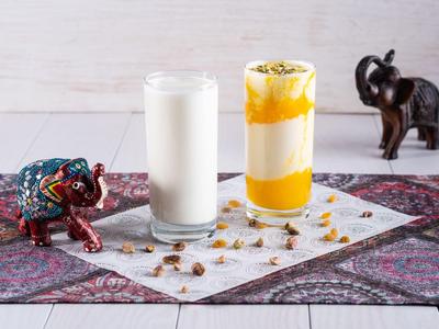 Zwei hohe Gläser mit weißer und gelber Flüssigkeit, umgeben von Dekorationen und Stoffstück.