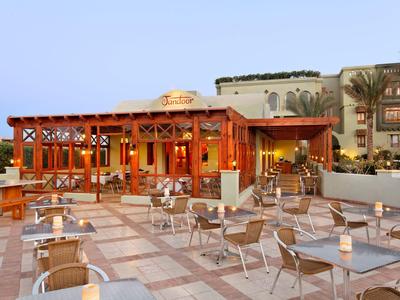 Außenbereich eines Restaurants mit Holzkonstruktion und Sitzplätzen auf gepflastertem Boden.