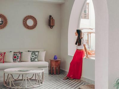 Frau mit rotem Rock lehnt an einem Fenster in einem modernen, hellen Zimmer mit Sofa.