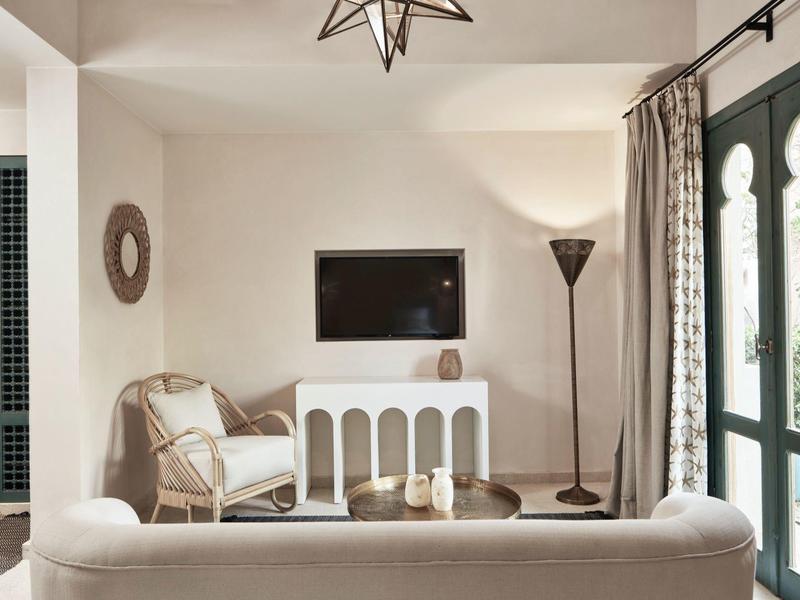 Heller Wohnzimmerraum mit weißem Sofa, Sessel, stehendem Lampenlicht und Wandfernseher.