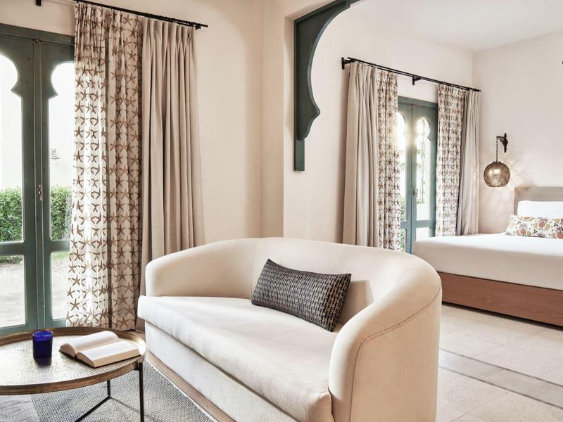 Helles Wohnzimmer mit cremefarbener Couch, schwarzem Kissen, rundem Holztisch und großem Spiegel.