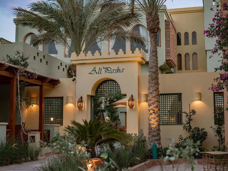 Haus mit mediterraner Architektur, Palmen und warmen Außenbeleuchtungen bei Abenddämmerung.