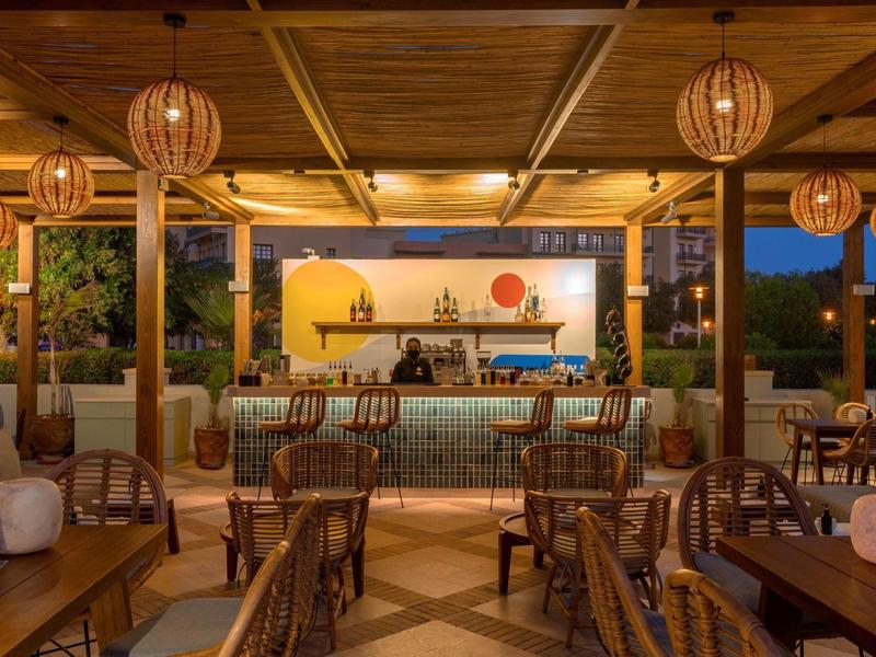 Offenes Restaurant mit Holzdecke, Korbstühlen und warmem Licht in der Abenddämmerung.