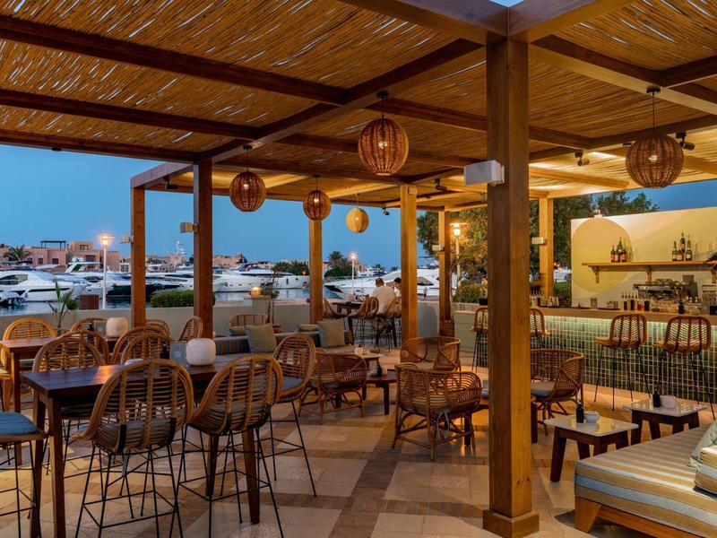 Offene Terrasse mit Holzdach, Tischen und Stühlen bei Dämmerung am Wasser gelegen.