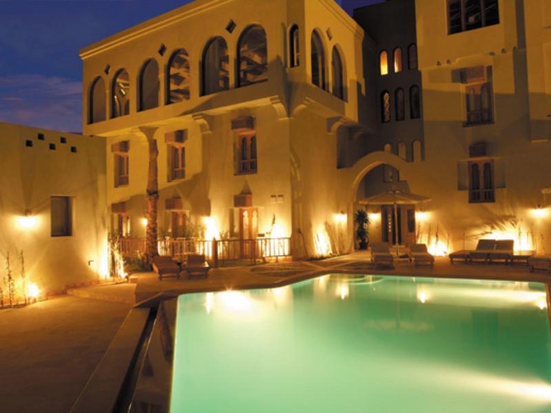 Beleuchtetes Gebäude mit architektonischen Bögen und einem ruhigen Pool bei Dämmerung.