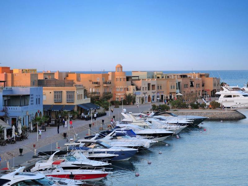 Hafen mit vielen Booten, modernem Kai und Gebäuden unter blauem Himmel bei Sonnenuntergang.