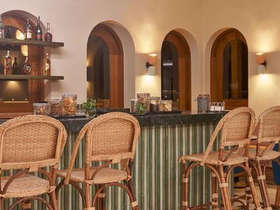 Gemütliche Hotelbar mit Korbstühlen und warmem Licht unter Bogenfenstern.