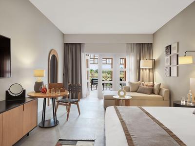 Geräumiges Hotelzimmer mit modernem Design, Doppelbett, Sitzbereich und Zugang zu Balkon mit Meerblick.