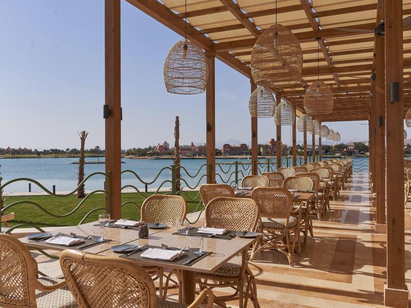 Außenrestaurant mit Korbstühlen und Holzdach, Blick auf ruhigen Fluss und grüne Ufer.