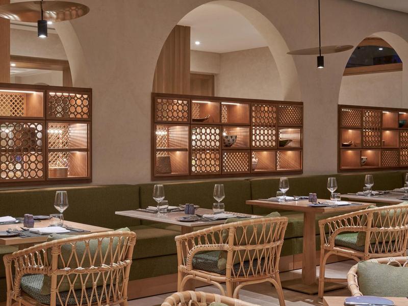 Restaurant mit Holztischen, geflochtenen Stühlen und warmen, architektonischen Rundbögen.