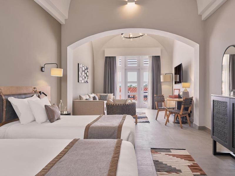 Helles Hotelzimmer mit zwei Doppelbetten, Sofa, Schreibtisch, Balkon und modernem Interieur.