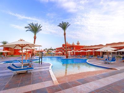 Moderner Hotelpool mit blauen Liegen und weißen Sonnenschirmen unter Palmen bei klarem Himmel.