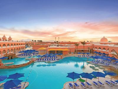 Großer Hotelpool bei Sonnenuntergang mit vielen blauen Sonnenschirmen und Liegestühlen.