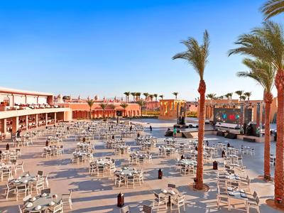 Großer Außenbereich mit vielen Tischen und Stühlen sowie Palmen unter klarem Himmel in einer Hotelanlage.