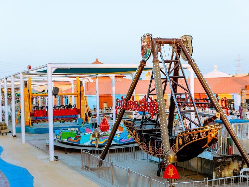 Freizeitpark mit Schiffsschaukel, bunten Karussells und Sitzbereichen im Freien.