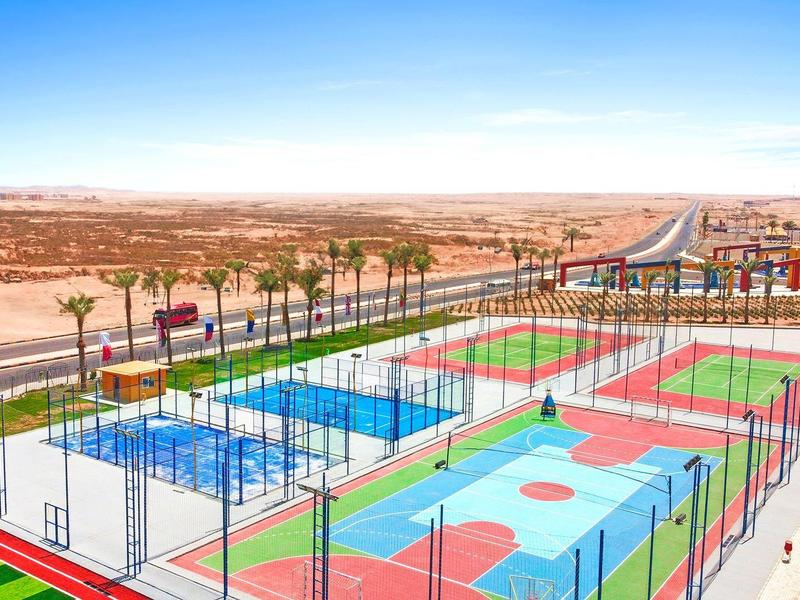 Bunte Sportplätze mit Tennis, Basketball und Volleyball in trockener Wüstenlandschaft.