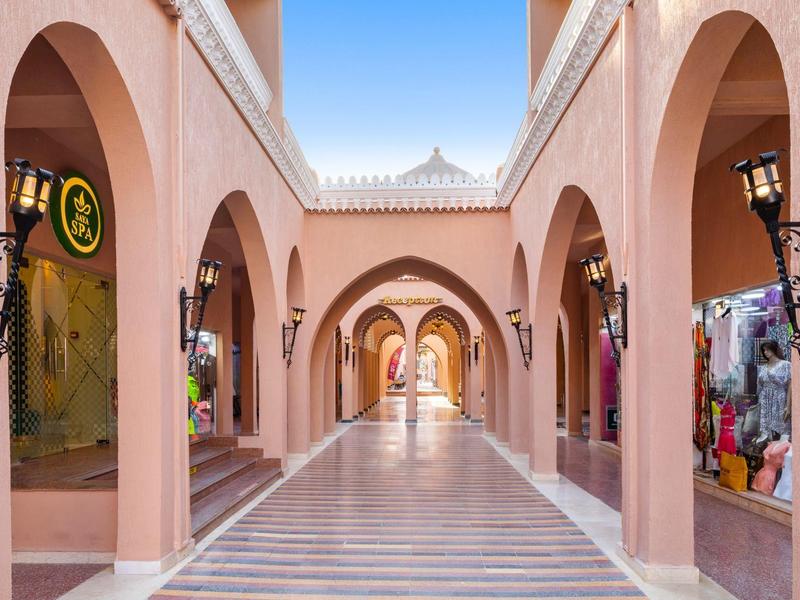 Ein langer Tunnel mit Rosa Bögen, Läden rechts und links und einem hellen Bodenmuster.