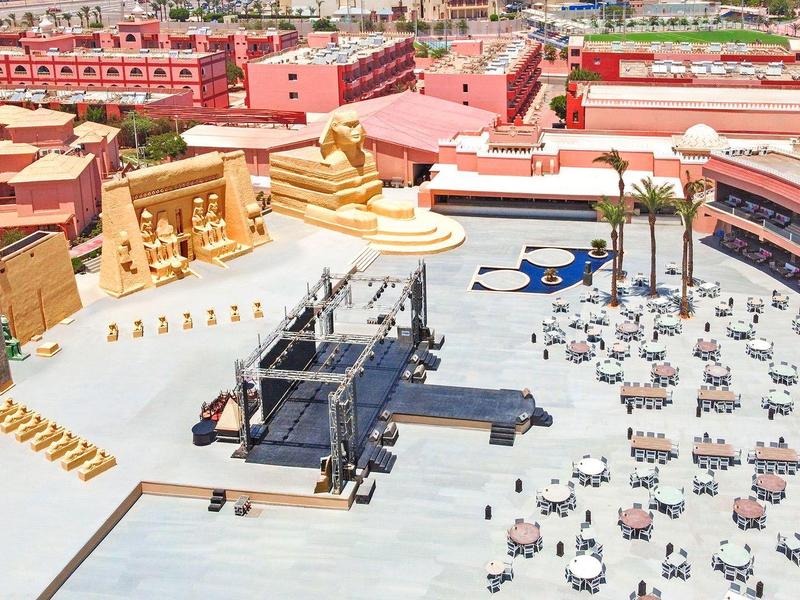 Großer Innenhof mit vielen Stühlen und Tischen, umliegend Häuser mit roten Dächern und gelben Wänden.