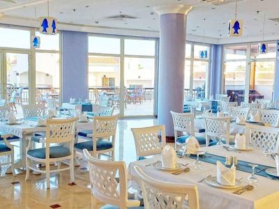 Helles, modernes Restaurant mit weißen Stühlen und blauen Akzenten, viele Fenster und Tageslicht.