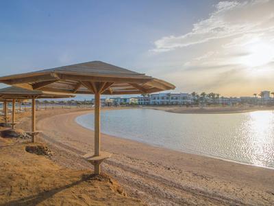 Leerer Sandstrand mit Sonnenschirmen und Blick auf ruhiges Wasser bei Sonnenaufgang.