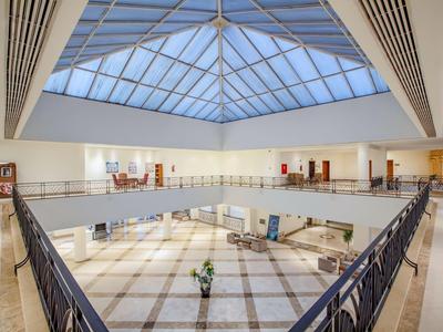 Helle Hotellobby mit großer Glasdecke, Marmorfußboden und moderner Einrichtung.