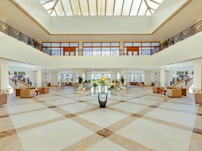 Große Hotel-Lobby mit viel Tageslicht, Sitzbereichen und Balkon auf der oberen Etage.