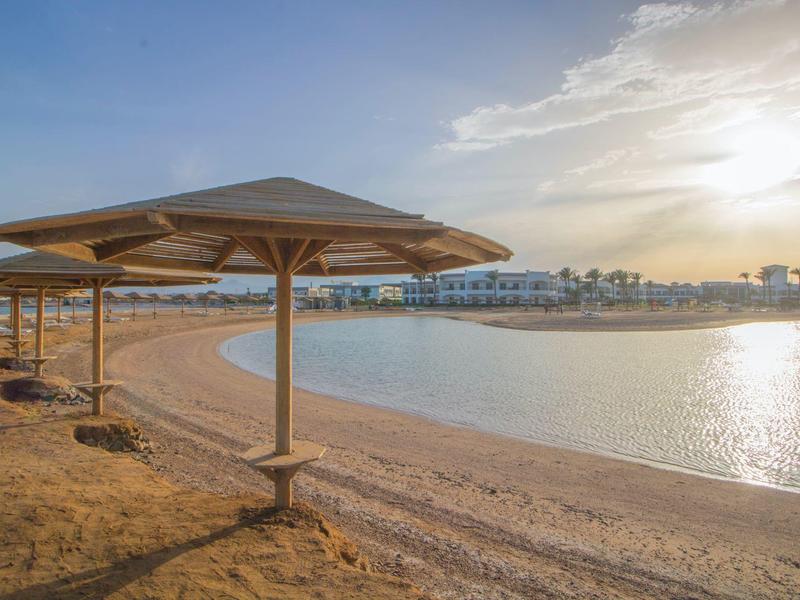 Leerer Sandstrand mit Sonnenschirmen und ruhigem Wasser bei Sonnenuntergang