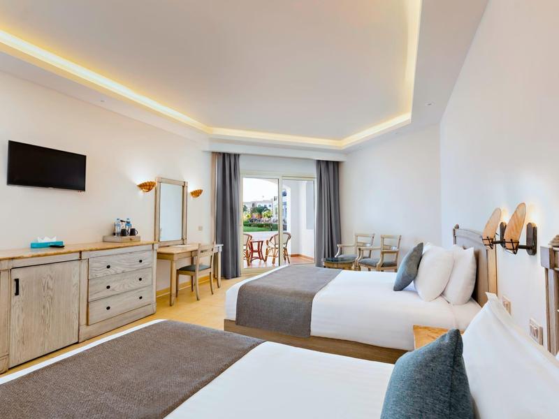 Modernes Hotelzimmer mit zwei Betten, Holzmöbeln, TV und Balkon mit Blick ins Grüne.