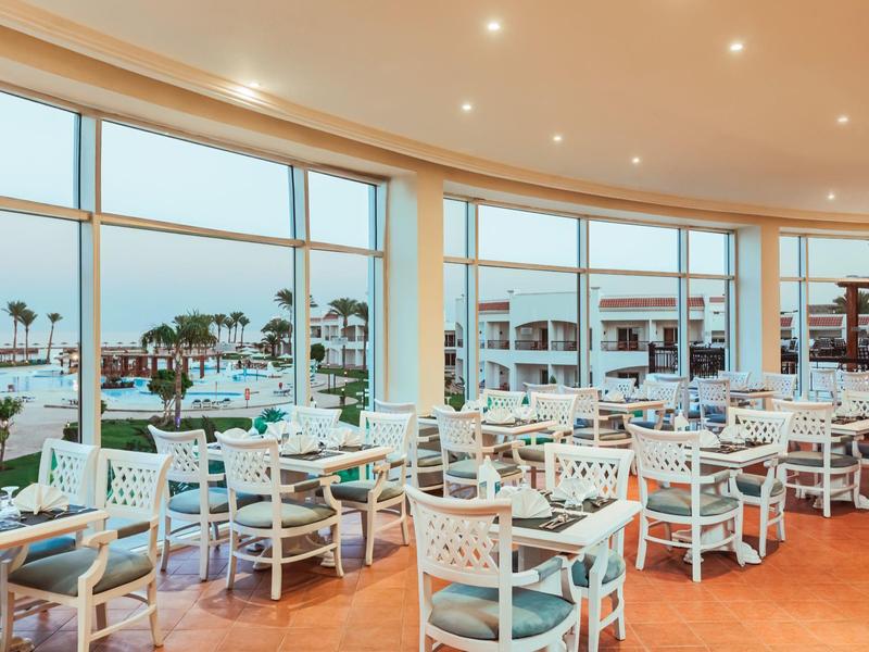 Helles, modernes Restaurant mit großen Panoramafenstern und weißen Stühlen mit blauen Kissen.