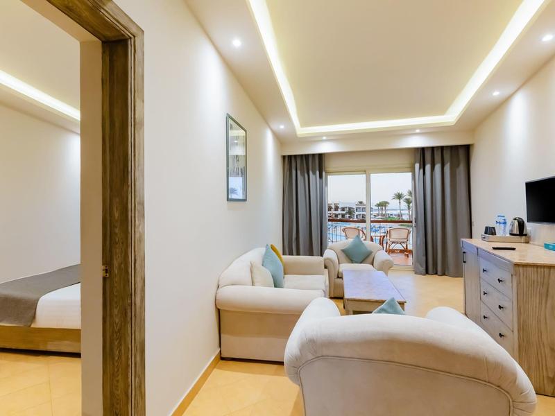 Modernes Wohnzimmer mit gemütlichem Sofa, TV, Holzkommode und Blick ins Schlafzimer mit großem Fenster.