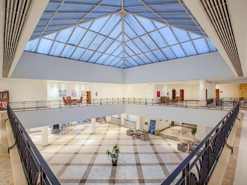 Helle Hotellobby mit großer Glasdecke, Marmorfußboden und moderner Einrichtung.