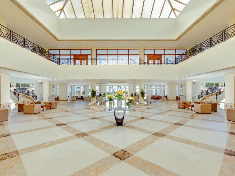 Helle, geräumige Hotellobby mit großer Glasdecke und Sitzbereichen auf beiden Seiten.