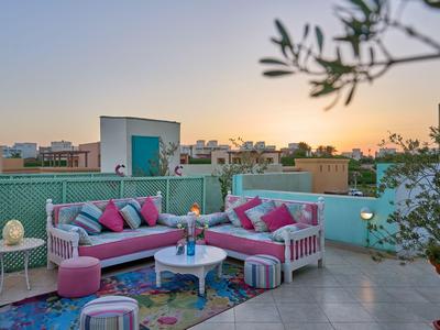 Gemütliche Dachterrasse mit pinker Lounge-Ecke, Pflanzen und Blick auf Stadt bei Sonnenuntergang.