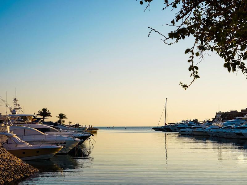 Ruhiger Hafen mit Segel- und Motorbooten bei Sonnenuntergang, klarer Himmel, spiegelndes Wasser.