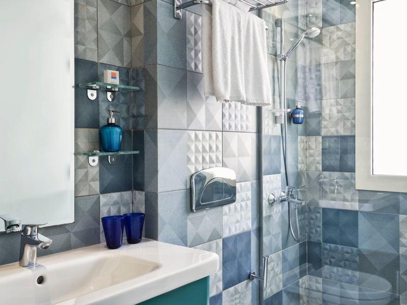 Modernes Badezimmer mit blauen Wandfliesen, Glasdusche, weißem Waschbecken und Handtüchern am Handtuchhalter.
