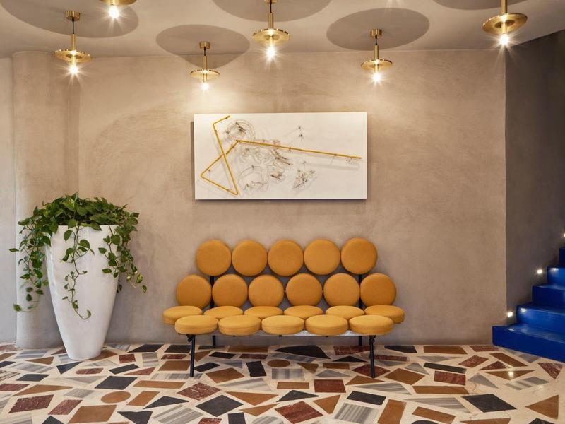 Modernes Wohnzimmer mit orangefarbenem Sofa, großer Pflanze, abstraktem Bild und blauen Treppen.