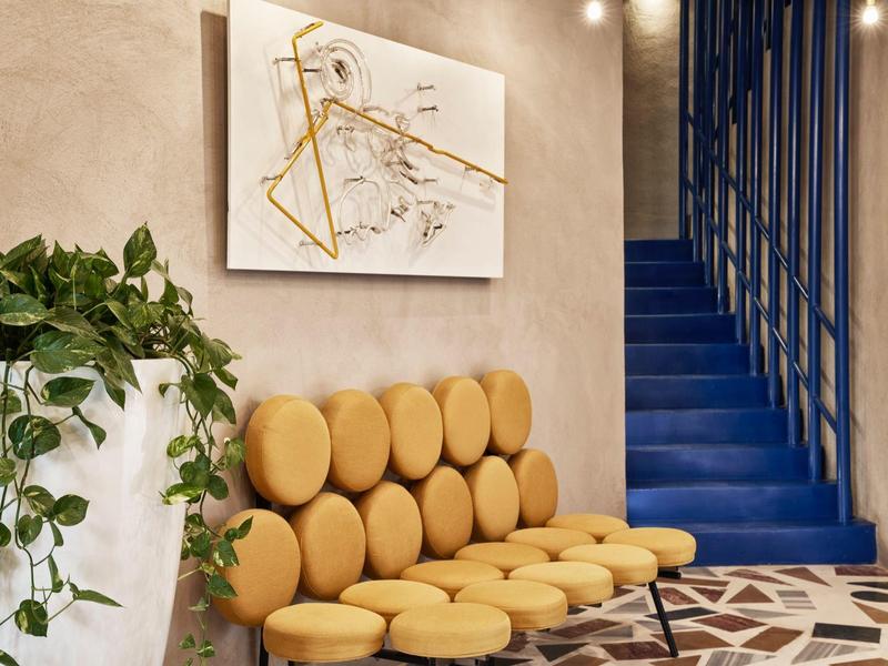 Moderner Wartebereich mit gelben runden Sitzkissen, blauer Treppe und grünem Pflanzenständer.