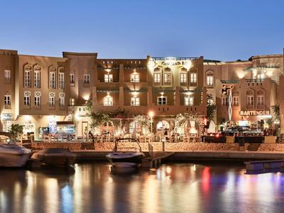 Illuminated hotel building by the water with boats and reflections at night.