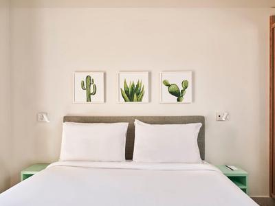 Simple double bed with white pillows, minimalist nightstands, and cactus prints on the wall.