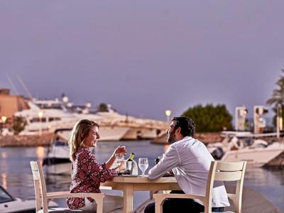 Couple sitting at a table by the harbor at sunset enjoying drinks.