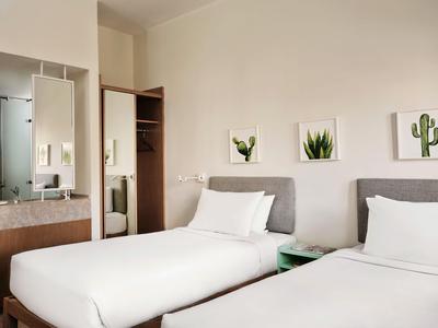 Simply furnished double room with two single beds, nightstand, and plant pictures on the wall.